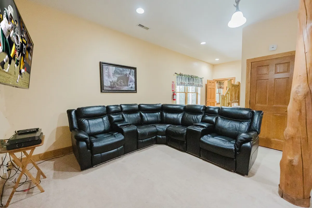 A cozy corner of the game room with a large leather sectional sofa facing a TV that’s playing a sports game, framed artwork on the walls, and a relaxed, comfortable atmosphere. The soft seating invites guests to settle in for movie night or cheer on their team together.