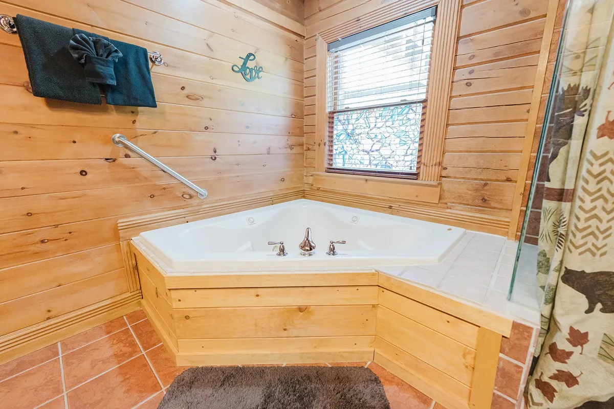 A tranquil bathroom retreat with a Jacuzzi tub, wood-paneled walls, a window streaming in daylight, decorative towels, and a 'love' sign. The setting is intimate and designed for total relaxation.