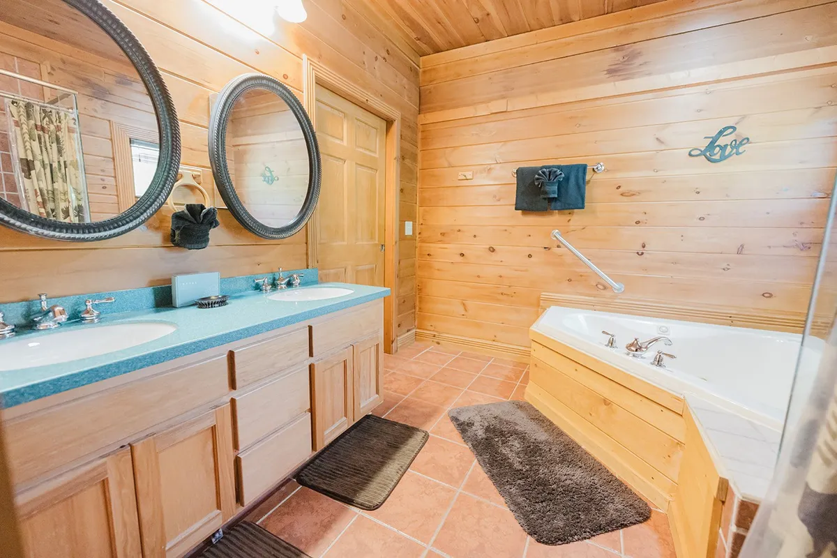 A serene bathroom with double sinks, spacious mirrors, a bathtub, and warm wood paneling. The area is flooded with natural light, ideal for relaxing routines and self-care after a day of adventure.