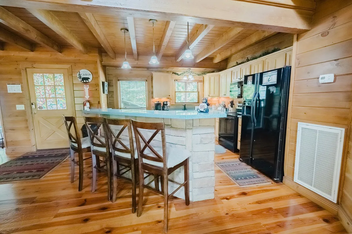 A bright, modern kitchen with a spacious island, bar stools for extra seating, wooden cabinetry, and large windows. The open design and ample counter space invite guests to participate in meal prep or casual breakfasts.