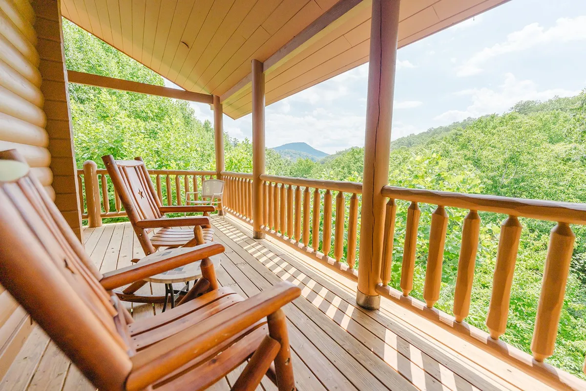 This image features classic wooden rocking chairs lined up on a wooden deck, looking out over a breathtaking mountain view. The peaceful setting is framed by a sturdy wooden railing, with lush greenery and distant peaks visible in the background, inviting quiet moments of relaxation and connection with nature.