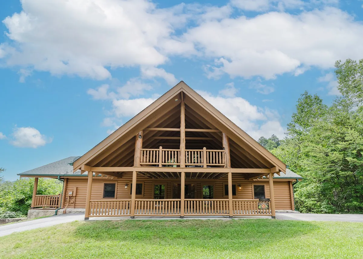 A welcoming log cabin with a spacious balcony, surrounded by greenery. The image captures the rustic charm of the property and the inviting outdoor spaces ideal for group gatherings, relaxation, or planning adventures into nearby attractions.