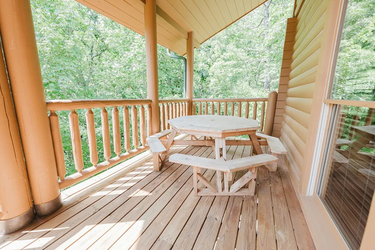 A charming view of a wooden picnic table set beside a log cabin, surrounded by lush greenery. The rustic setting highlights opportunities for al fresco dining, relaxing with a book, or sharing a quiet meal in the fresh mountain air.