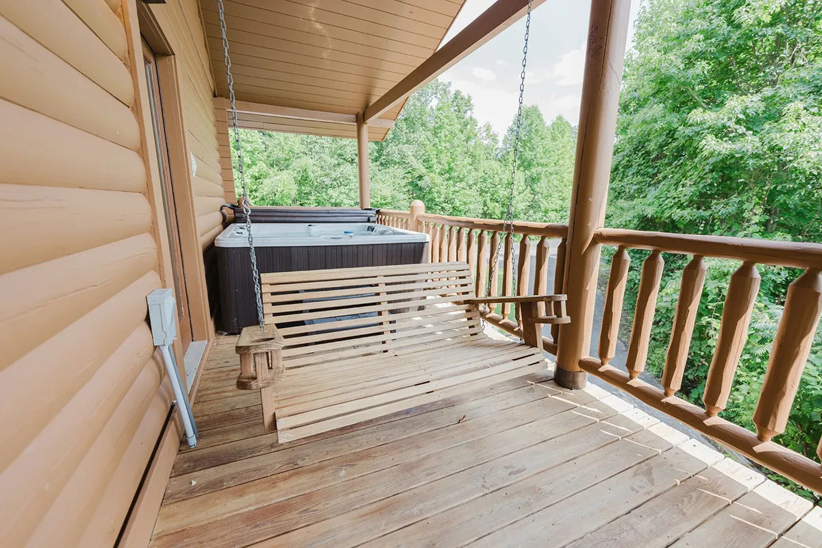 A tranquil deck space featuring a wooden swing bench and hot tub, set against a backdrop of vibrant forest greenery. The swing and hot tub are positioned for maximum enjoyment of the views, and the area exudes a sense of peaceful retreat and intimate connection with nature.